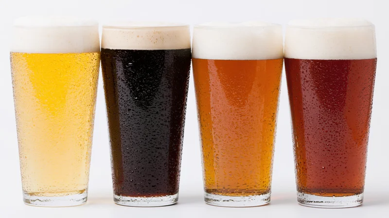 Four pint glasses of different beer varieties lined up in a row on white background