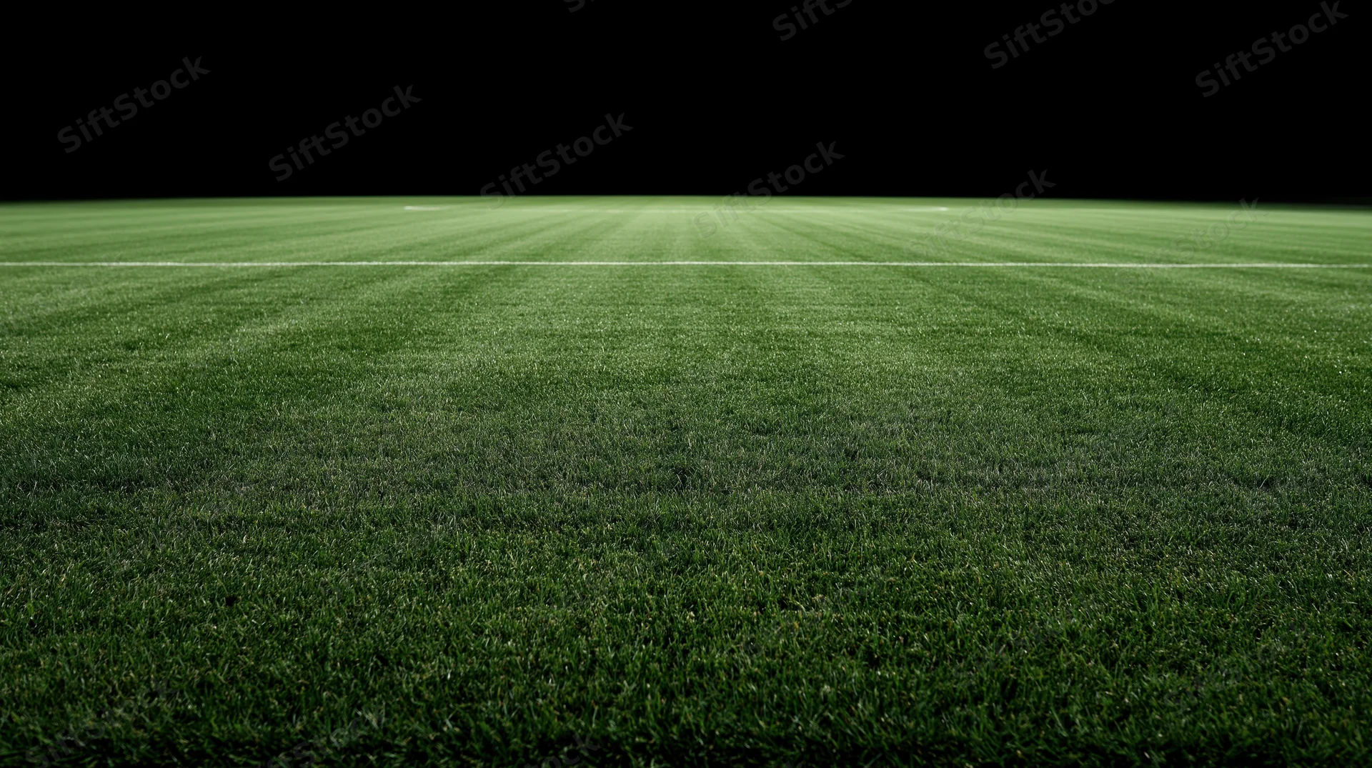 Freshly mowed grass field of a football stadium at night with a white boundary line and dark sky above