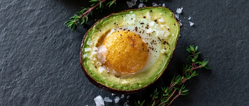 Baked egg in halved avocado on slate with thyme and flaky salt