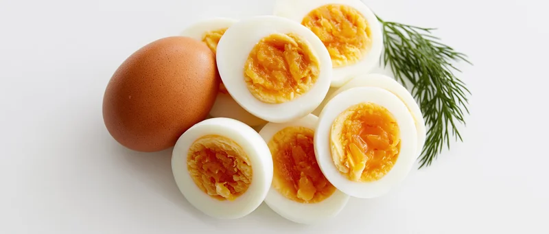 Hardboiled egg halves and whole egg arranged with dill on white surface