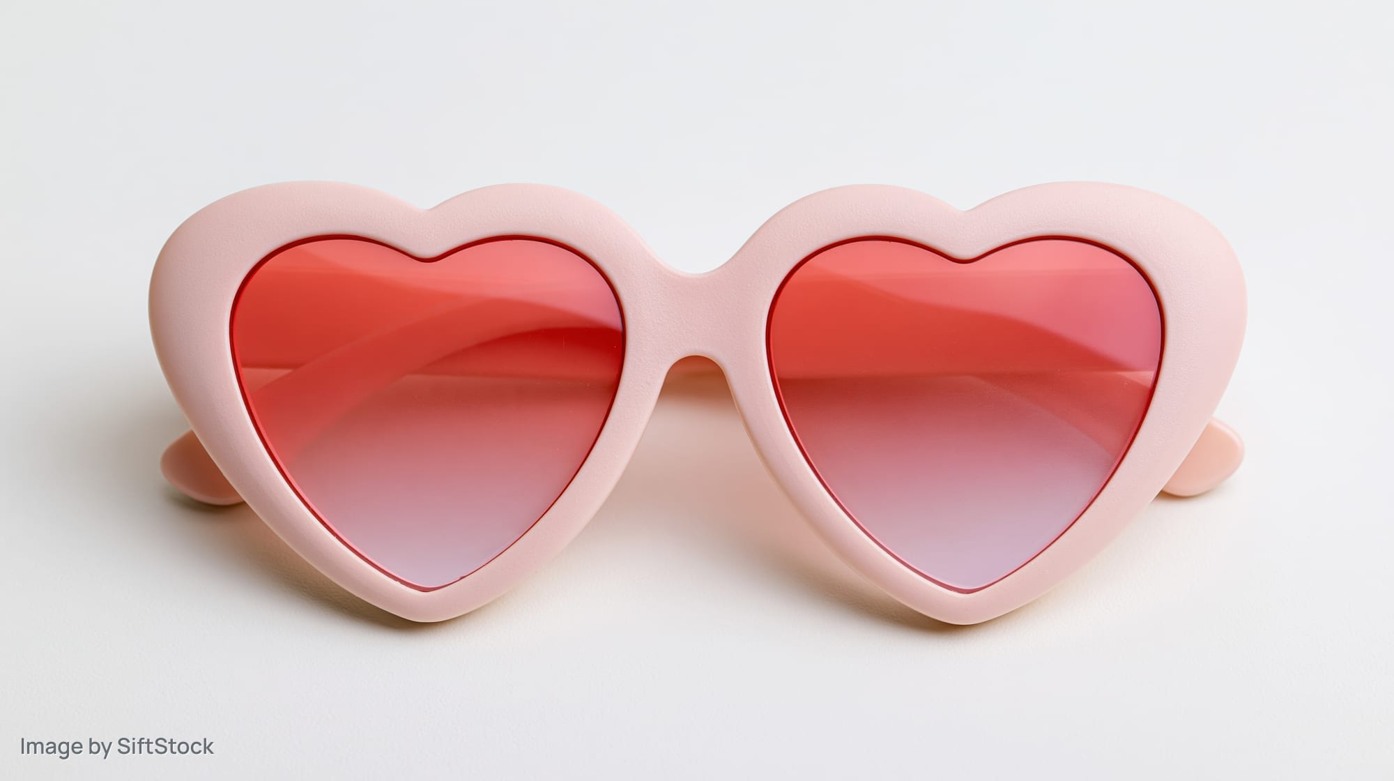 Heart-shaped sunglasses with pink plastic frames on white background