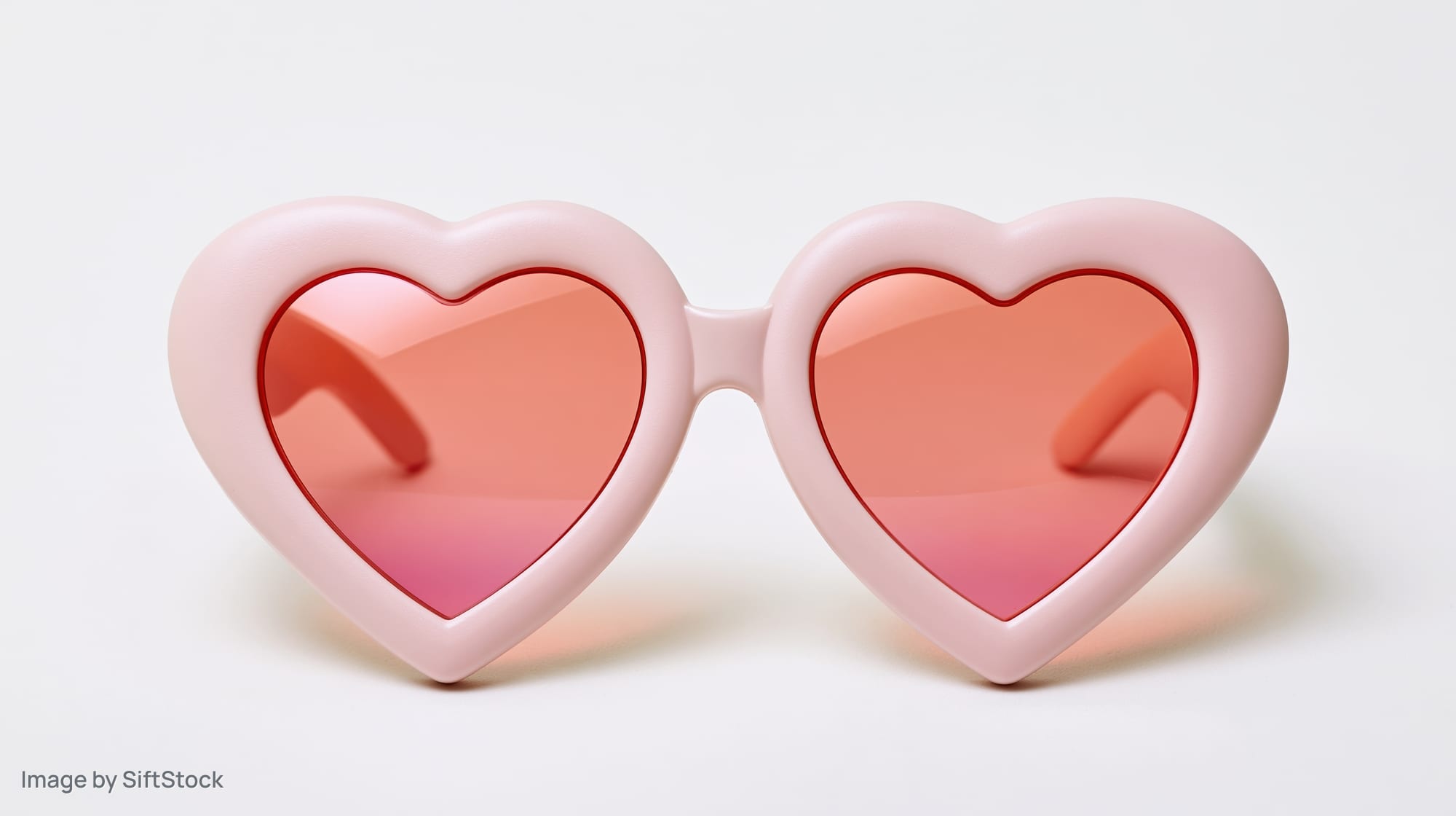 Heart-shaped novelty sunglasses with pale pink plastic frames on white background
