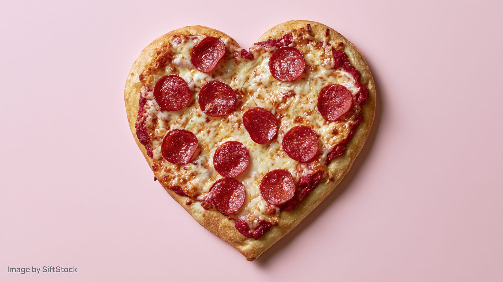 Heart-shaped pepperoni pizza with melted cheese and tomato sauce on pink background