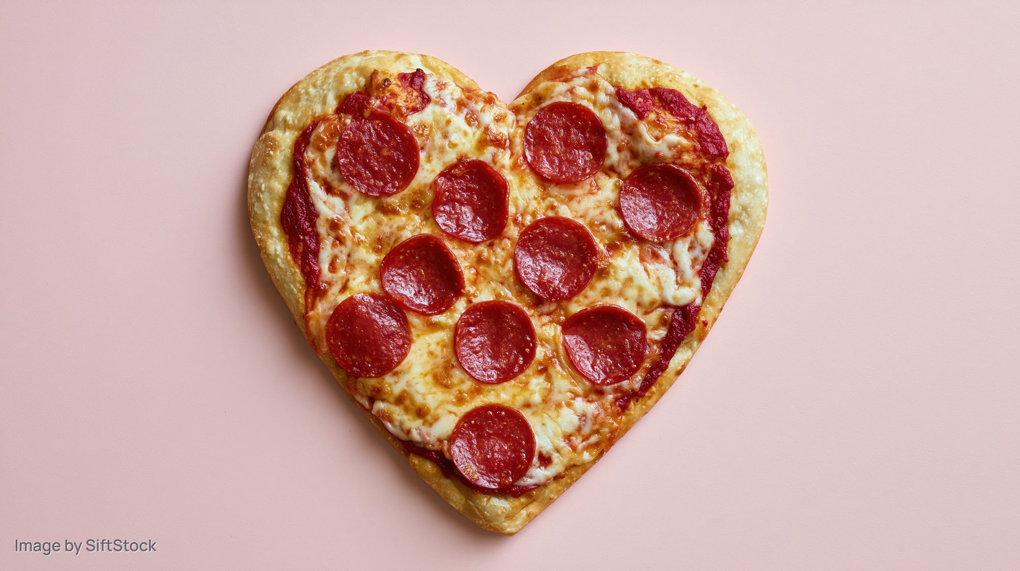 Heart-shaped pepperoni pizza with melted mozzarella on pink background