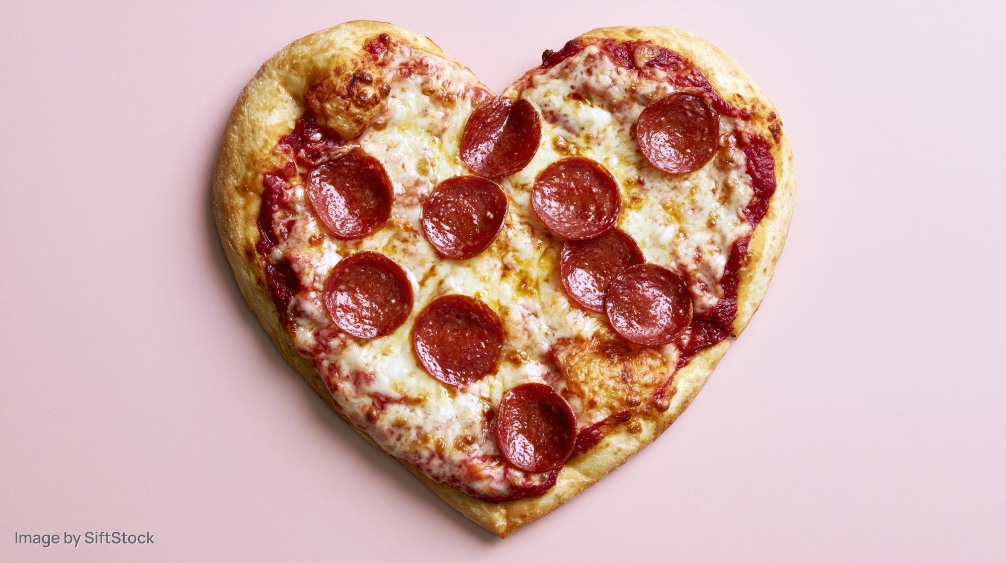 Heart-shaped pepperoni pizza with melted mozzarella on pink background