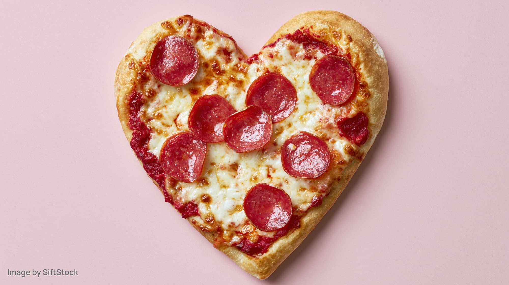 Heart-shaped pepperoni pizza with melted mozzarella on pink background