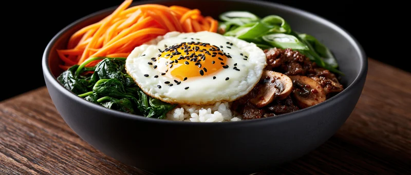 Korean bibimbap in a dark matte ceramic bowl with fried egg and vegetables on wooden surface