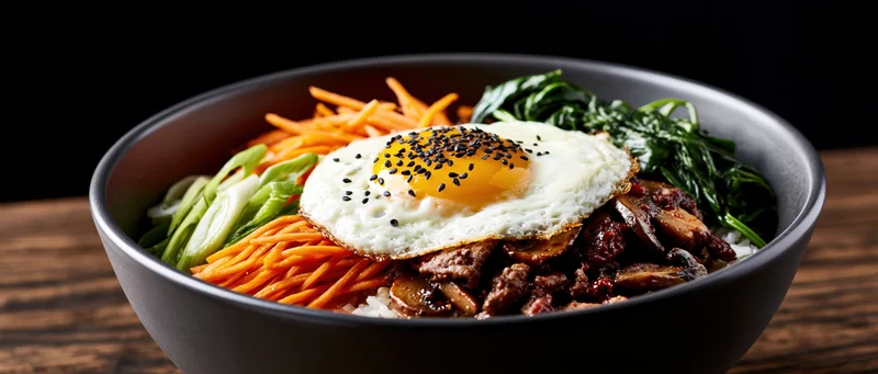 Korean bibimbap in a dark matte ceramic bowl topped with a fried egg and assorted vegetables on a wooden surface