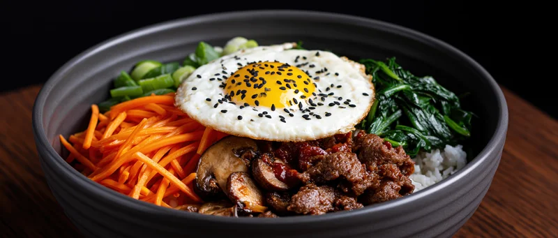 Korean bibimbap in a dark matte ceramic bowl with beef, vegetables, and a fried egg on top