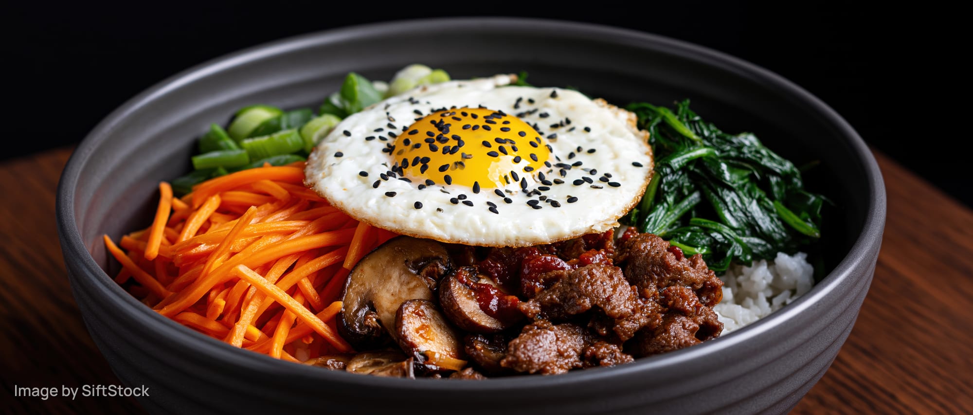 Korean bibimbap in a dark matte ceramic bowl with beef, vegetables, and a fried egg on top