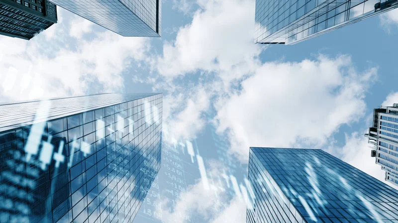 Low-angle view between glass skyscrapers under a cloudy blue sky