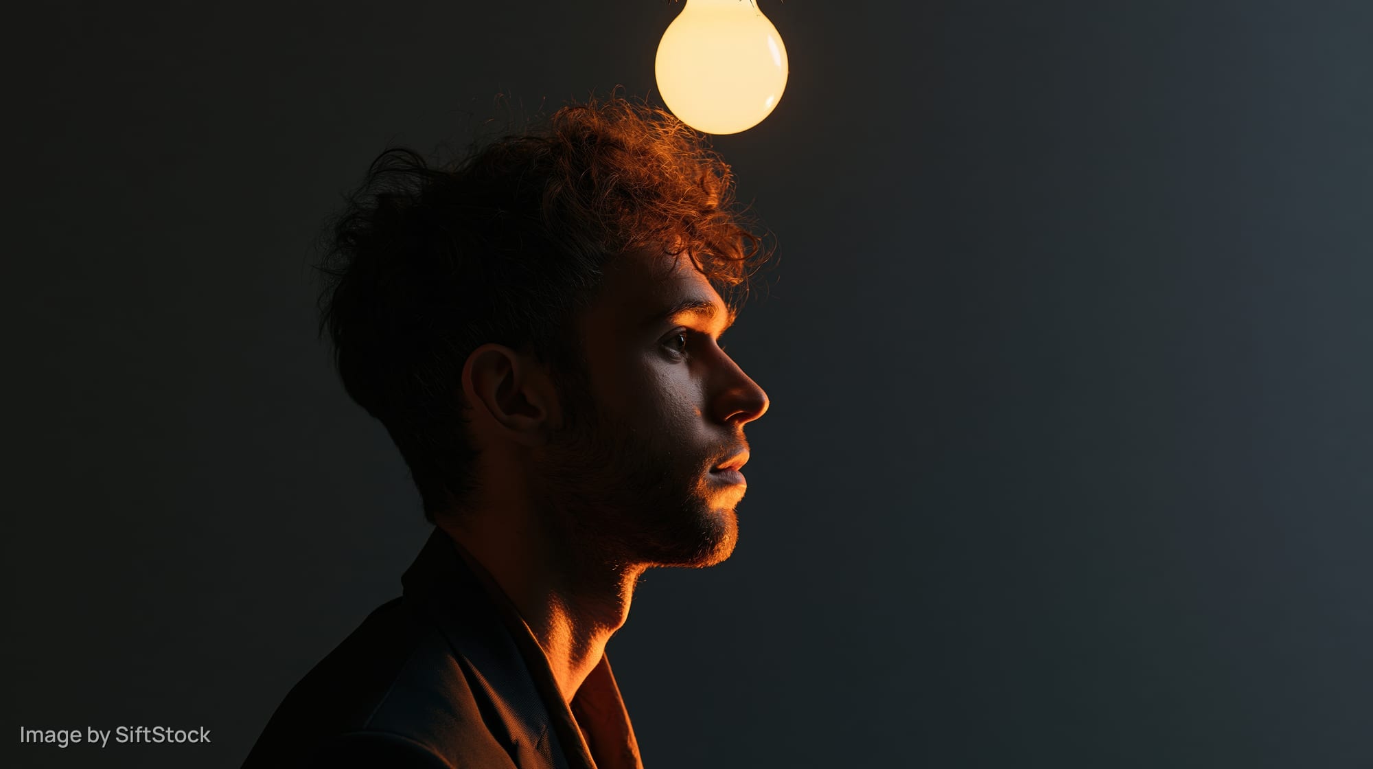 Man in profile silhouette with glowing lightbulb above his head against dark background