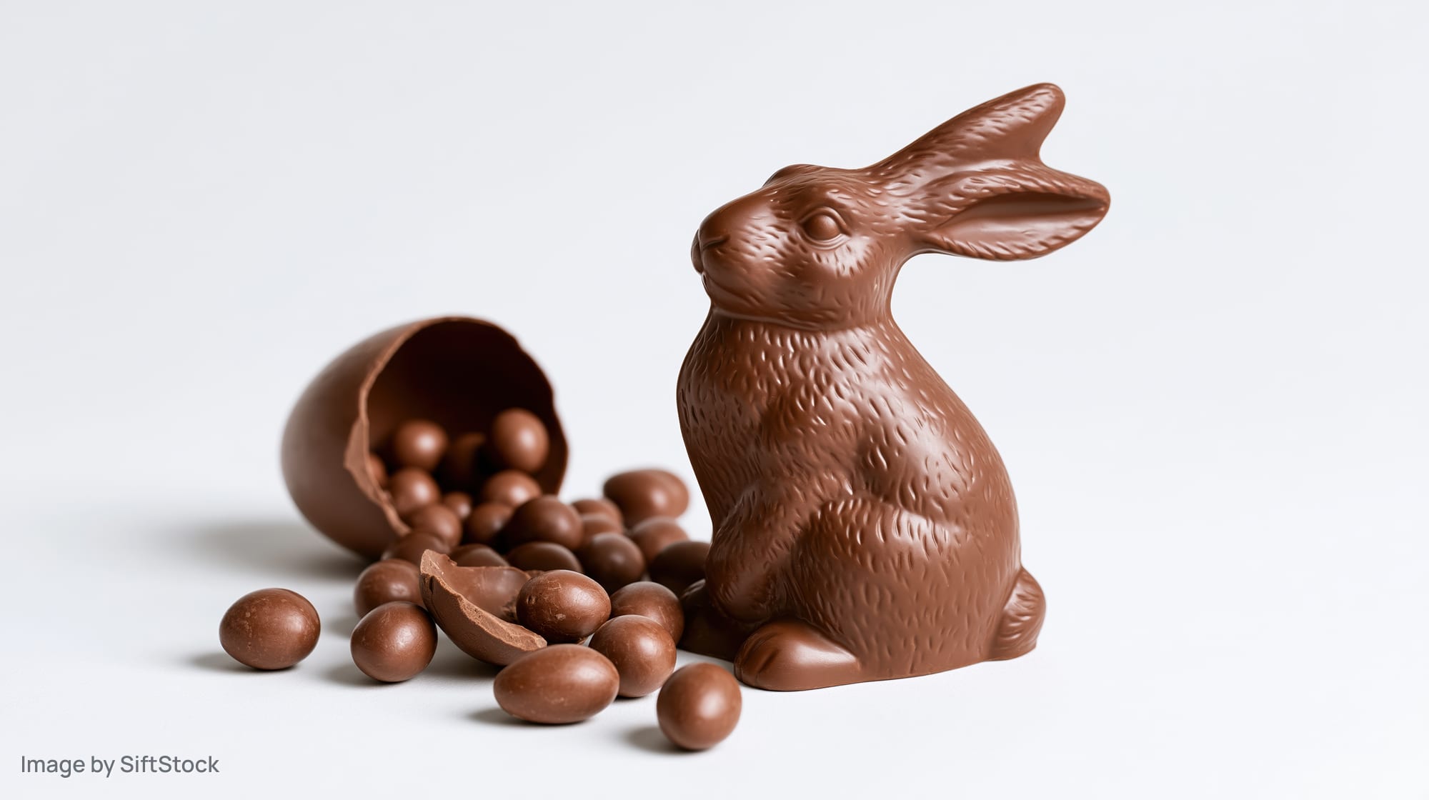 Chocolate easter bunny figurine with spilled chocolate eggs on white background