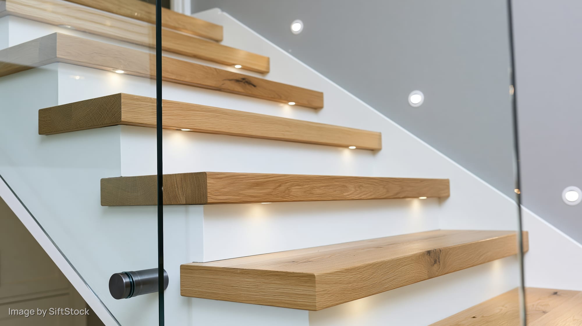 Modern wooden staircase with glass railing and recessed lighting in a white interior