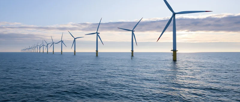 Row of wind turbines extending across open sea under cloudy sky