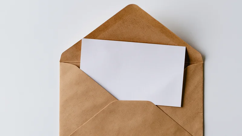 Open kraft paper envelope with blank white card inside, flat lay on white background