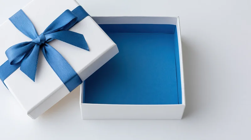 Open white gift box with blue ribbon bow and empty interior on white surface
