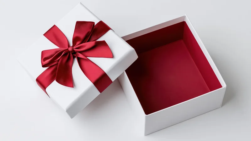 Open white gift box with red satin ribbon bow on lid resting beside empty interior on plain white surface