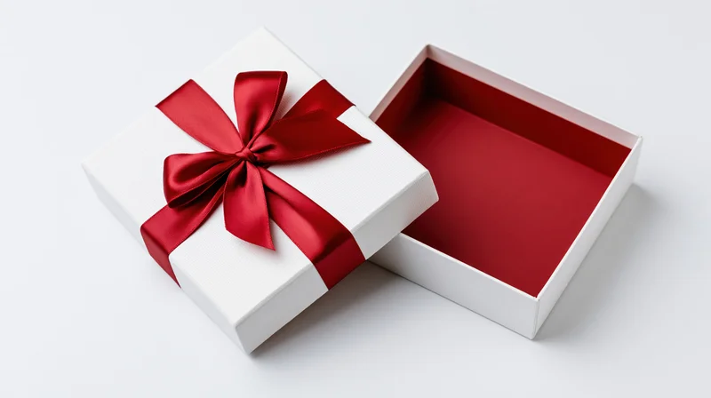 Open white gift box with red satin ribbon bow on lid resting beside empty interior on white surface