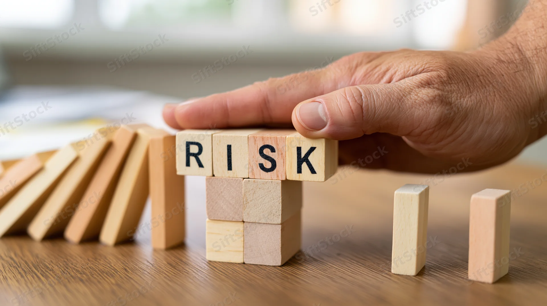 Hand stopping wooden blocks spelling risk on a desk