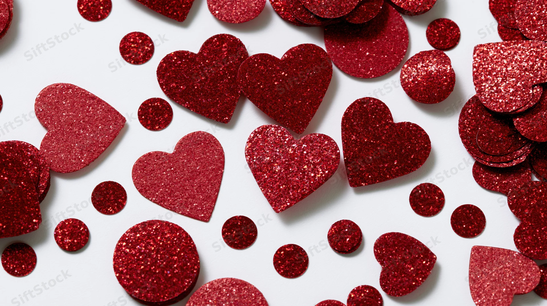 Red glitter hearts and circle confetti scattered on white background