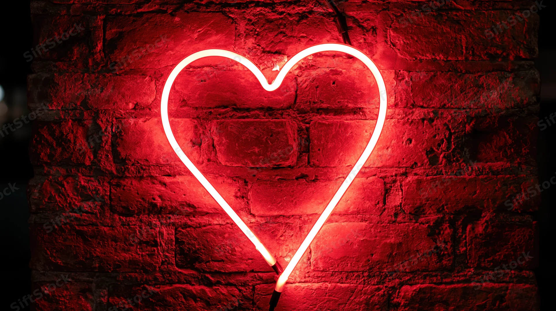 Red neon heart sign glowing on a dark brick wall