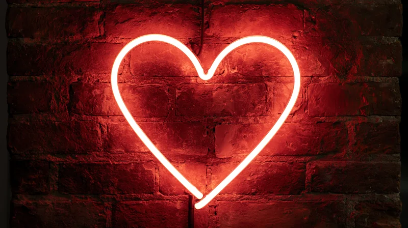 Red neon heart sign glowing on a dark brick wall