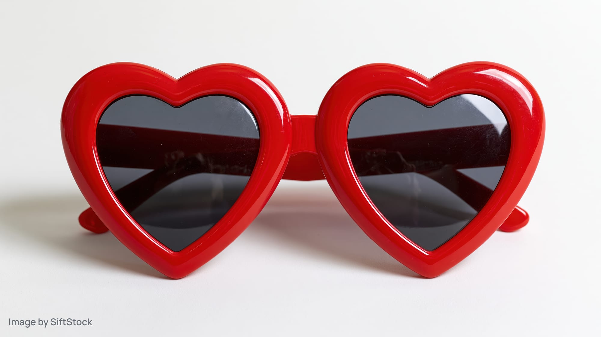 Red heart-shaped novelty sunglasses lying flat on white surface