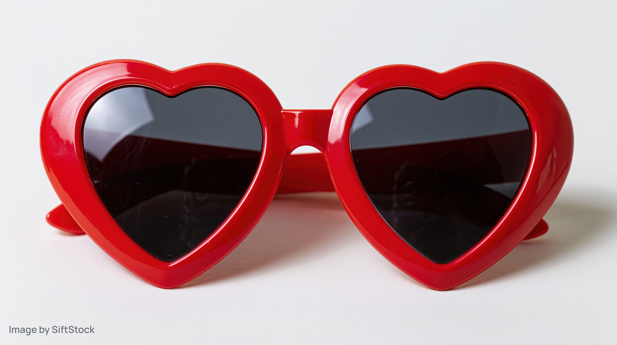 Red heart-shaped novelty sunglasses lying flat on white surface