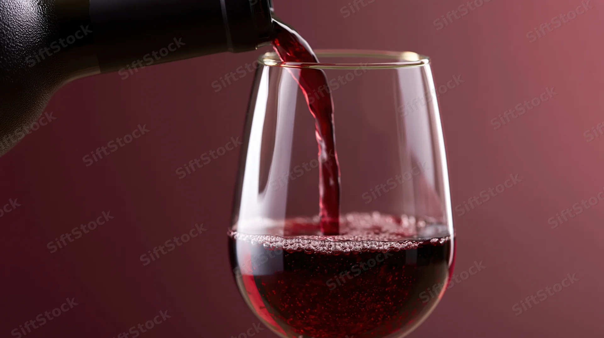 Red wine being poured from a dark bottle into a clear stemless glass