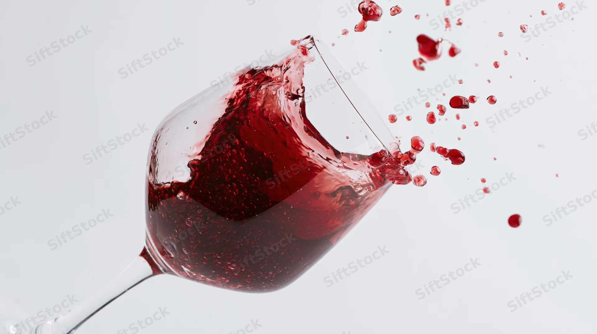 Red wine splashing dynamically in a tilted crystal wine glass against white background
