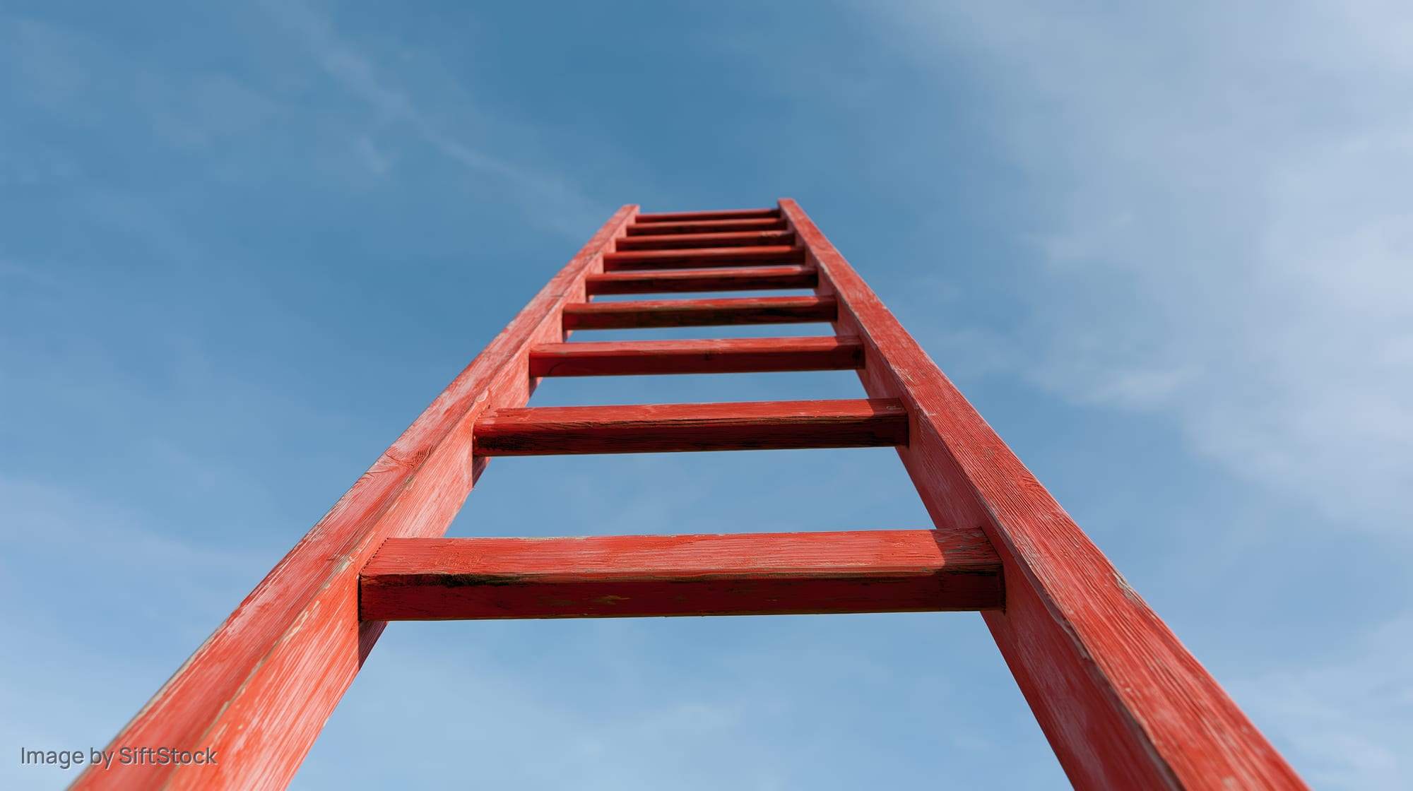 Red wooden ladder rising vertically into clear blue sky from low angle