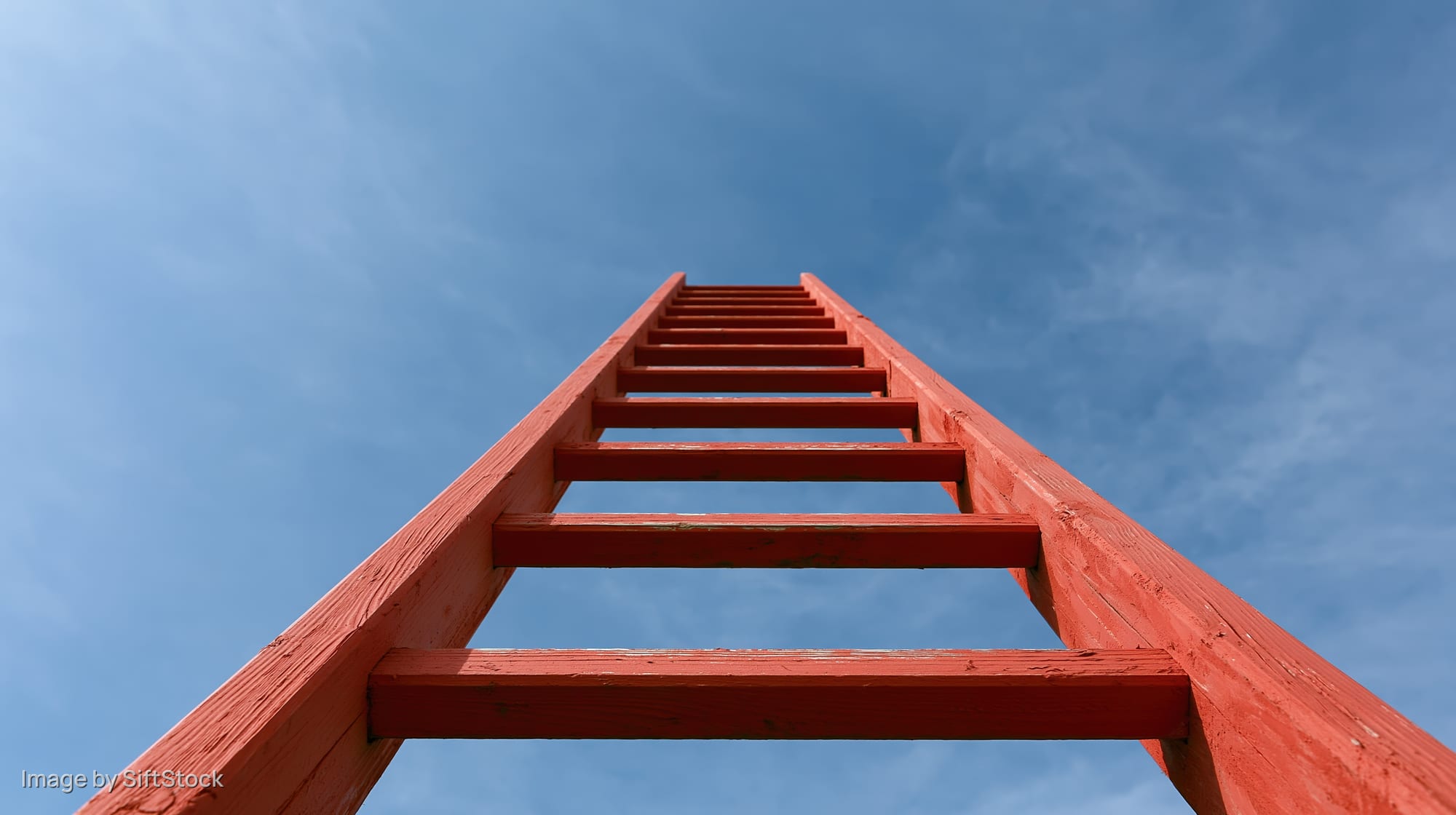 Red wooden ladder rising vertically into open blue sky viewed from below