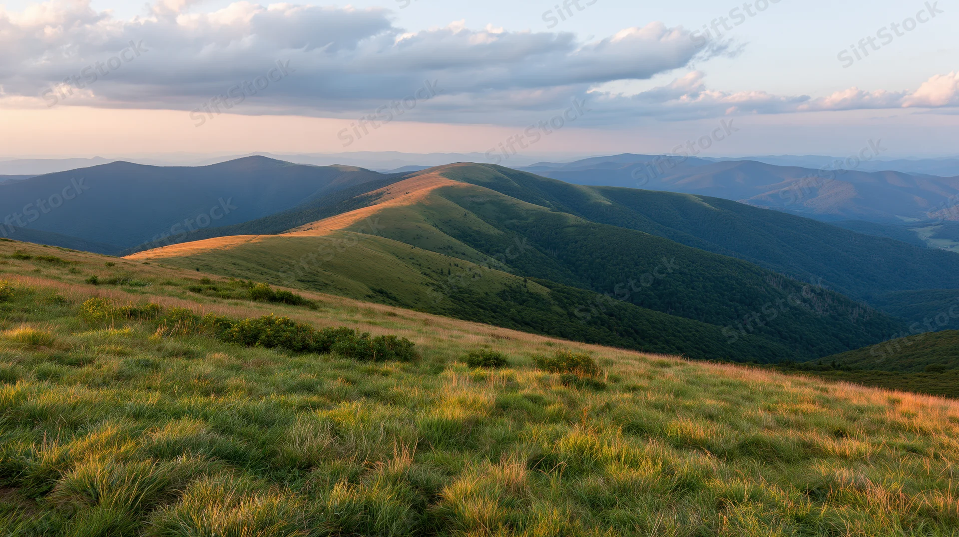 Rolling green mountain ridges under a partly cloudy sky at sunset