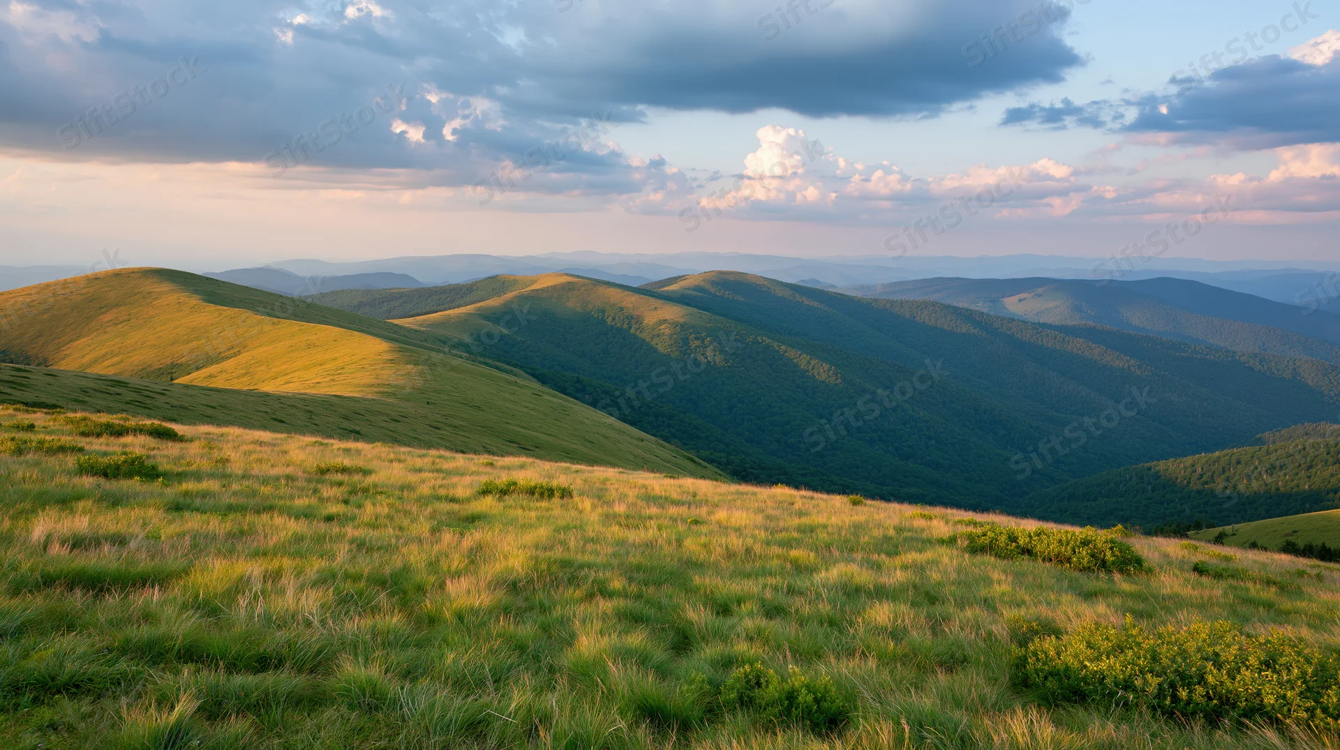 Rolling green mountain ridges under a dramatic partly cloudy sky at sunset