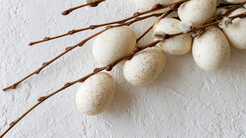 White speckled easter eggs with gold foil accents arranged on willow branches against a textured white wall