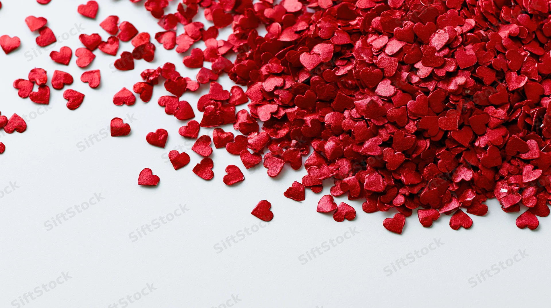 Red foil heart confetti scattered across a white surface with copyspace