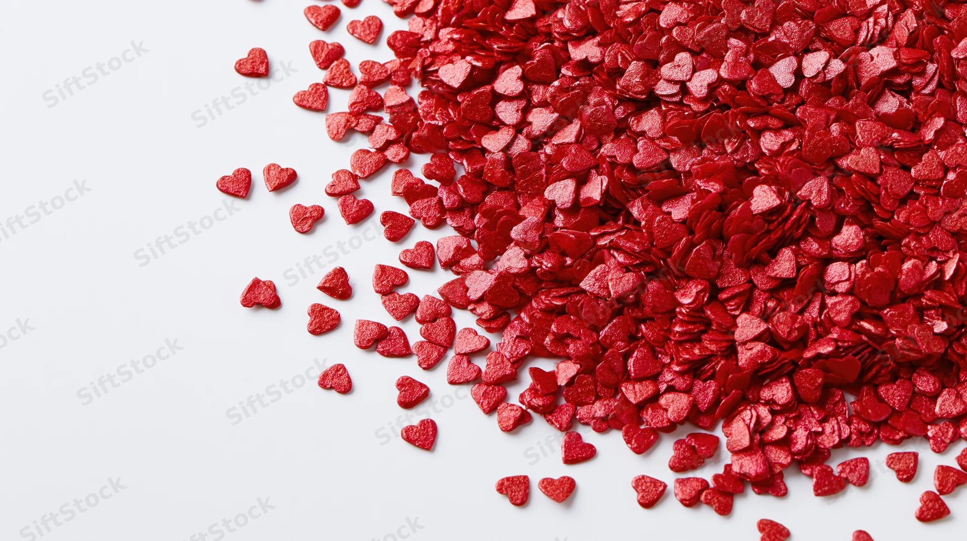 Red foil heart confetti scattered across a white surface with copyspace