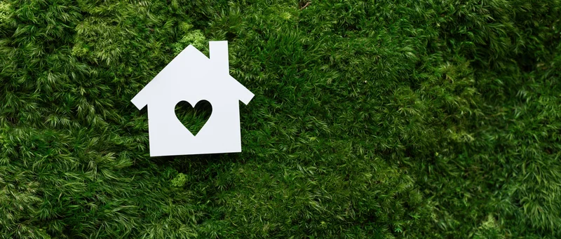 White paper house cutout with heart-shaped window on green moss background