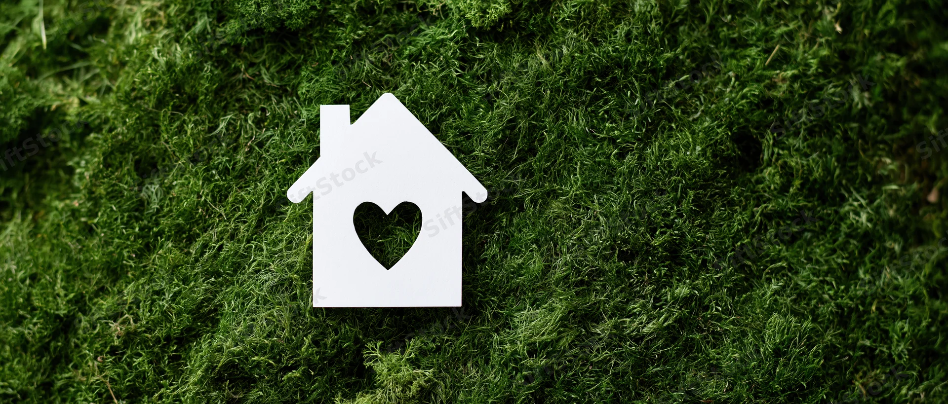 White paper house cutout with heart-shaped window on green moss surface