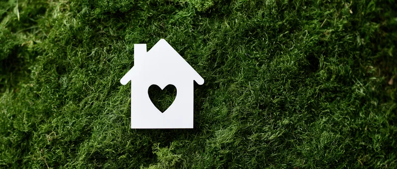 White paper house cutout with heart-shaped window on green moss surface
