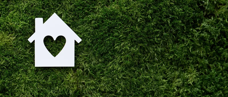 White paper house cutout with heart-shaped window on green moss background