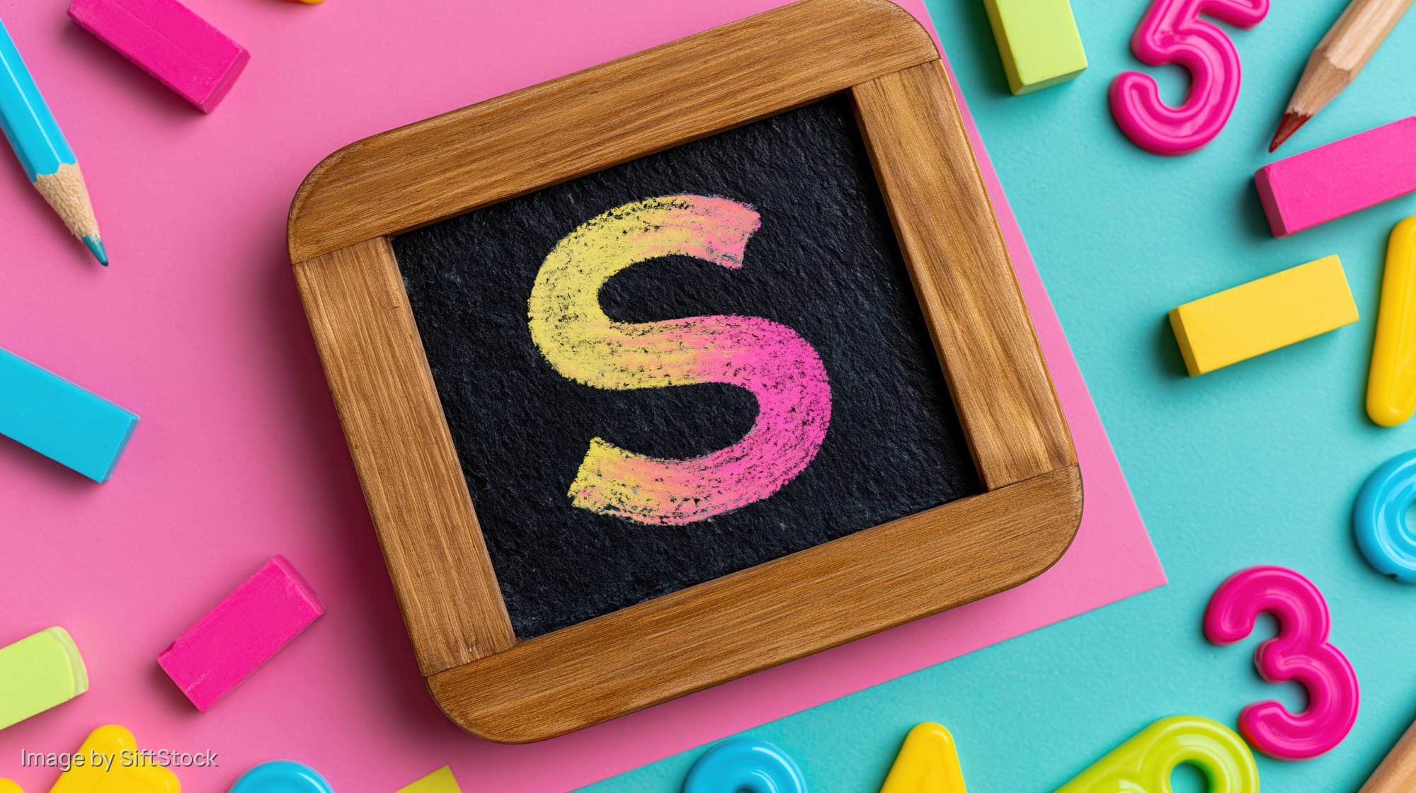 Wooden-framed chalkboard with chalk-drawn letter s surrounded by colorful school supplies on pink and blue background