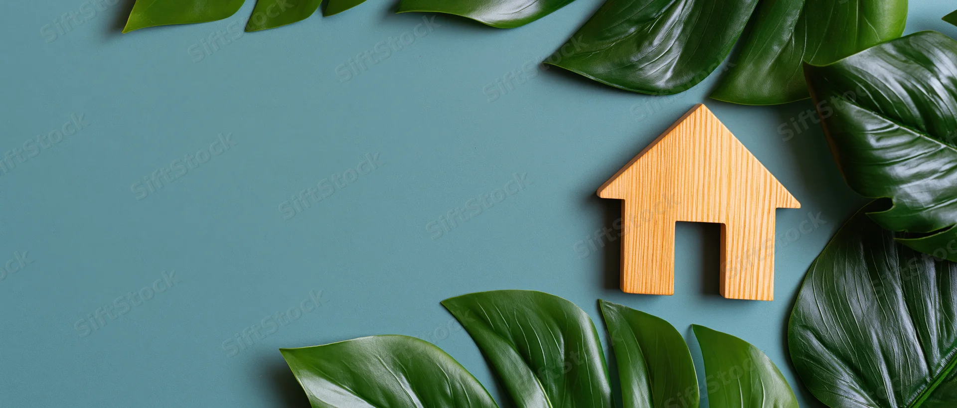 Wooden house cutout surrounded by monstera leaves on teal surface