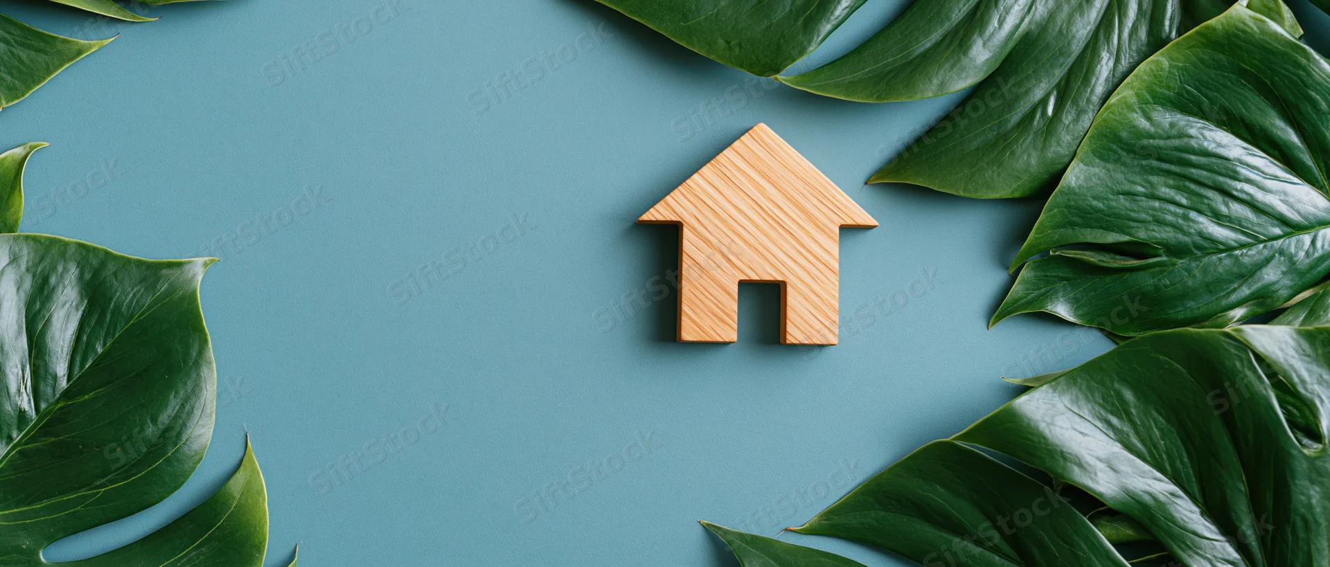 Wooden house cutout surrounded by monstera leaves on teal blue surface