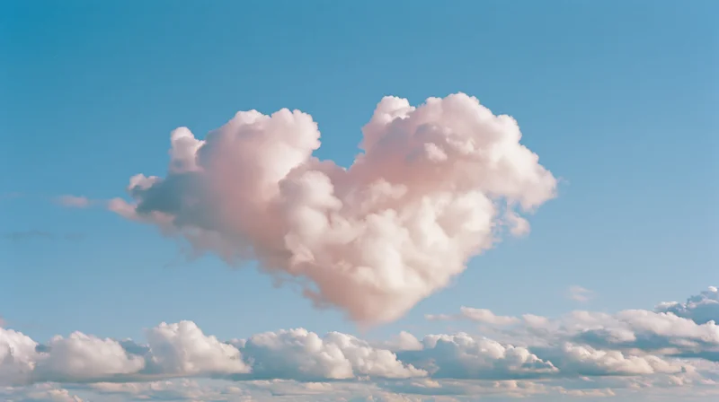 Heart-shaped cloud floating in a clear blue sky with soft pink and white cumulus formations