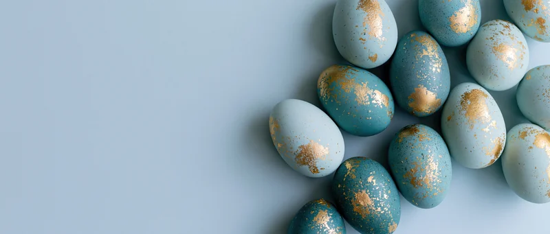 Blue and gold painted easter eggs arranged in a cluster on a light blue surface with copyspace