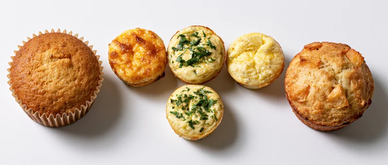 Six baked goods including muffins and savory egg bites arranged on a white surface