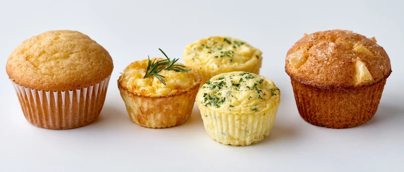 Five muffins of varying types arranged in a row on a white surface