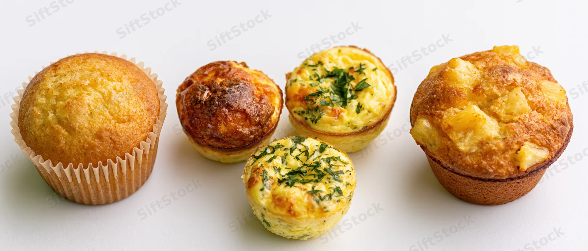 Five assorted muffins arranged in a row on a white background